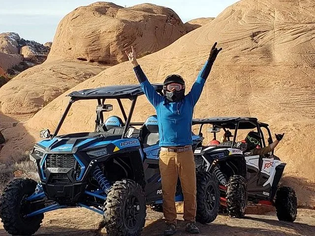 Eine Person posiert mit einem blauen Polaris RZR Buggy auf Slickrock-Gelände.