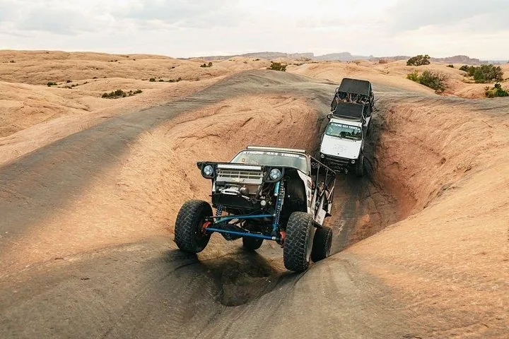 Two off-road vehicles navigating a steep slickrock descent in the desert.