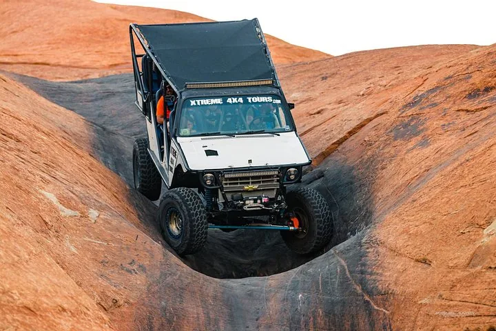 Off-road vehicle descending a steep narrow crevice on slickrock.