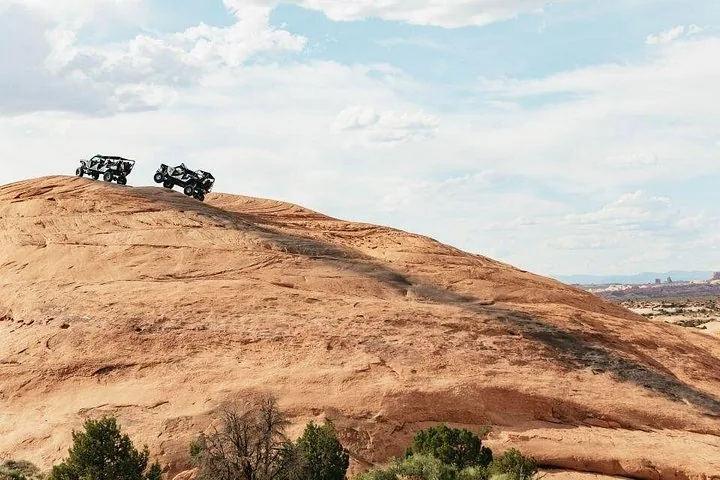 Two off-road vehicles traversing a large slickrock dome in the desert.