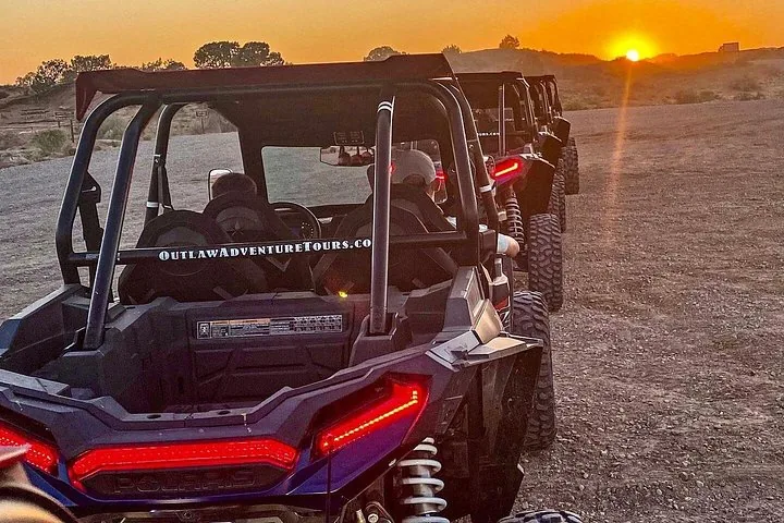 Eine Reihe geparkter UTV-Buggies auf einem unbefestigten Weg bei Sonnenuntergang.