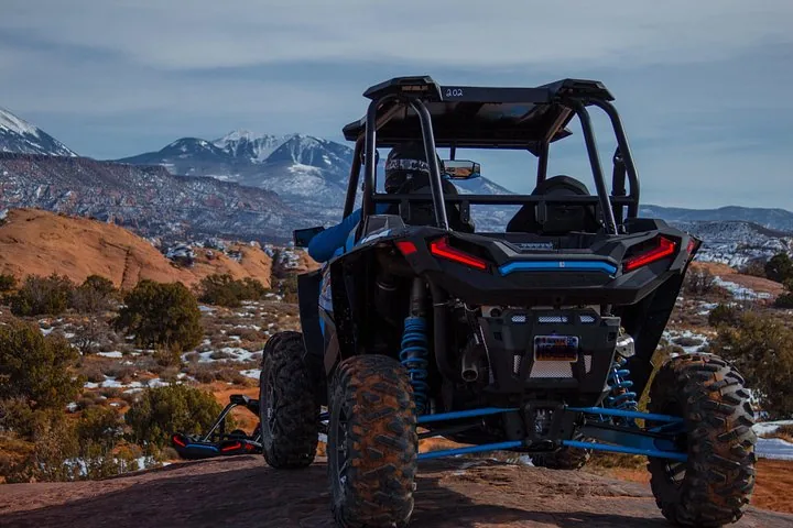 Vista trasera de un buggy Polaris azul mirando hacia montañas nevadas.