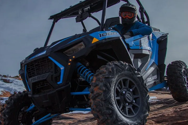 Primer plano de un Polaris RZR azul conducido sobre roca lisa con parches de nieve.