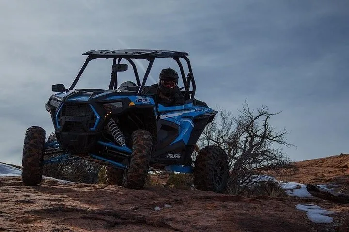 Ein blauer UTV-Buggy fährt bei bewölktem Himmel über rotes Slickrock-Gelände.