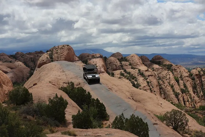 Ein Offroad-Fahrzeug erklimmt bei bewölktem Himmel eine steile, enge Felsformation.